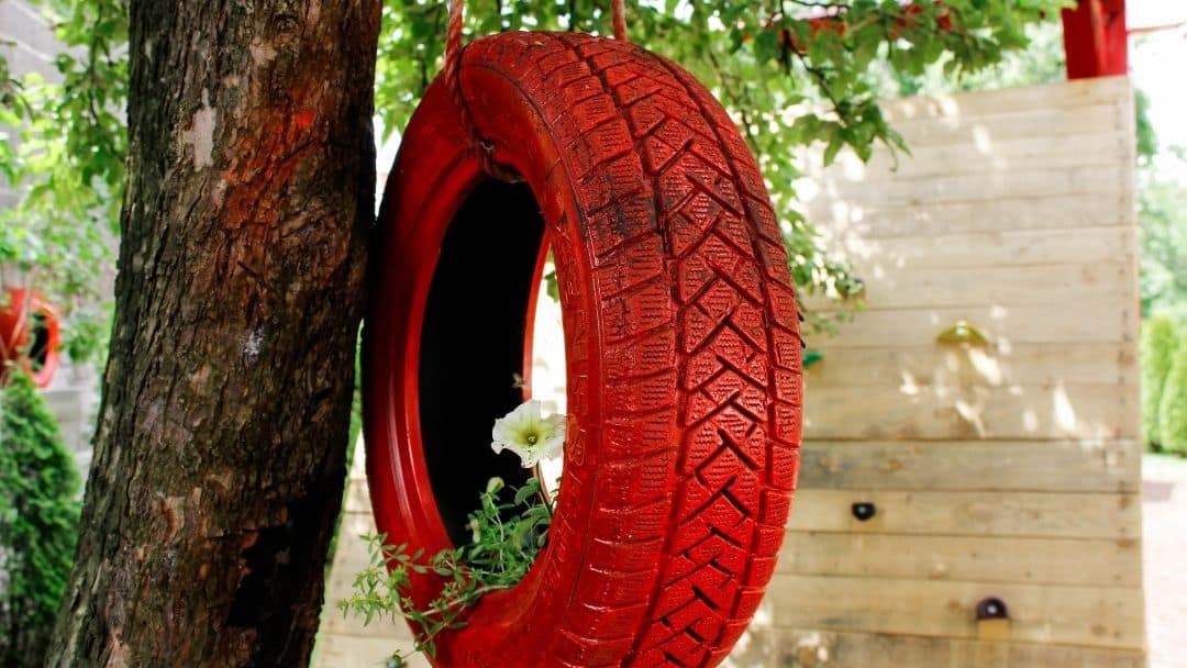 A tire painted red and hanging from a tree with flowers growing inside.