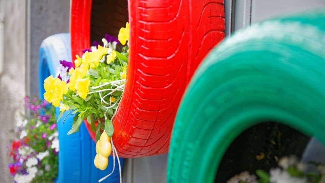 Three hanging painted DIY tire planters with flowers growing